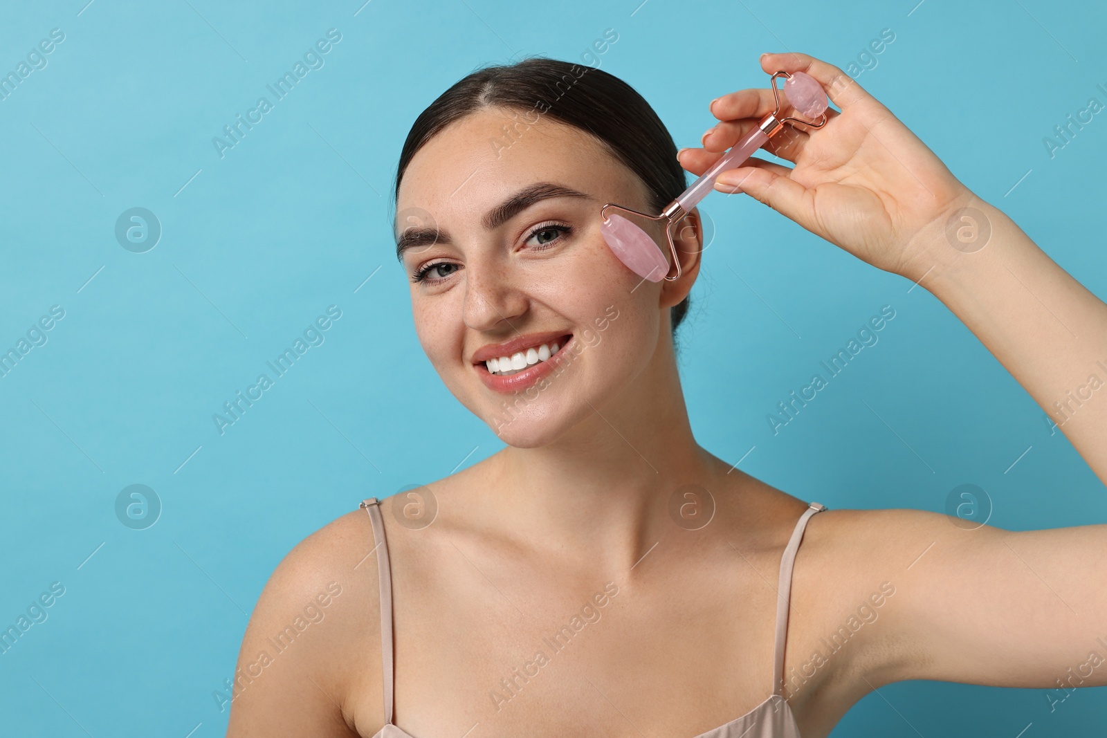 Photo of Beautiful young woman doing facial massage with roller on light blue background