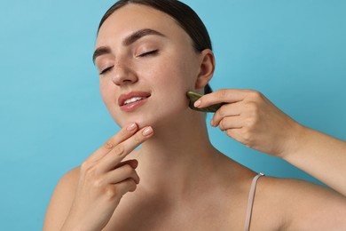 Photo of Beautiful young woman doing facial massage with gua sha tool on light blue background