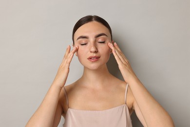 Photo of Face massage. Beautiful young woman with healthy skin on grey background