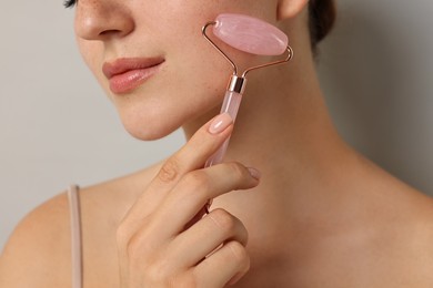 Woman doing facial massage with roller on light grey background, closeup