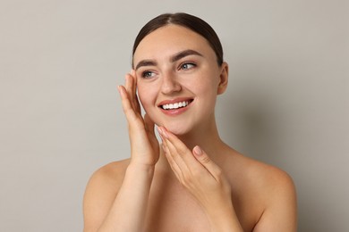 Beautiful young woman with healthy skin on grey background