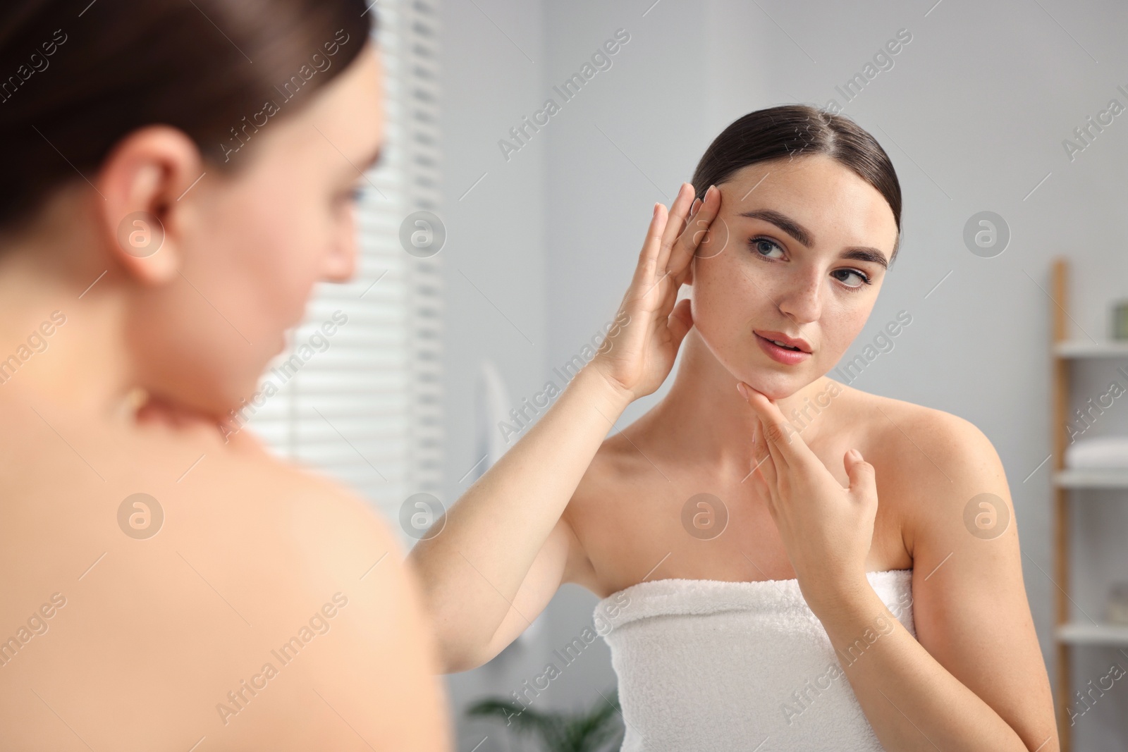 Photo of Beautiful young woman doing facial massage near mirror at home