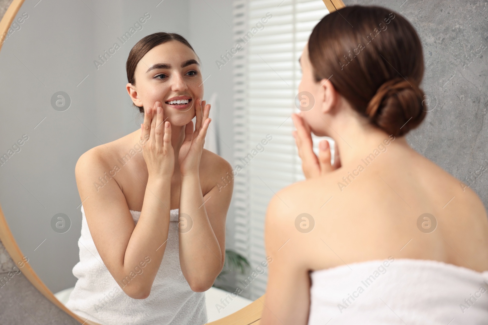 Photo of Beautiful young woman doing facial massage near mirror at home