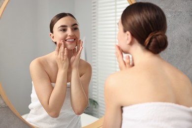 Photo of Beautiful young woman doing facial massage near mirror at home