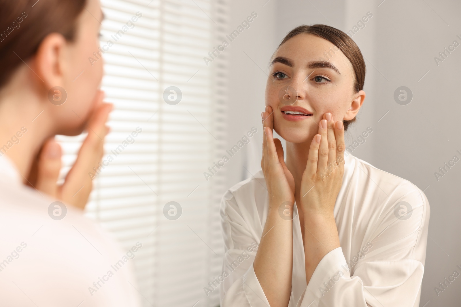 Photo of Beautiful young woman doing facial massage near mirror at home