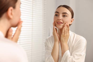 Beautiful young woman doing facial massage near mirror at home