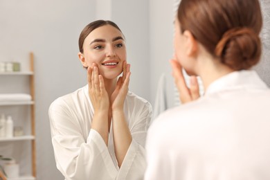 Photo of Beautiful young woman doing facial massage near mirror at home