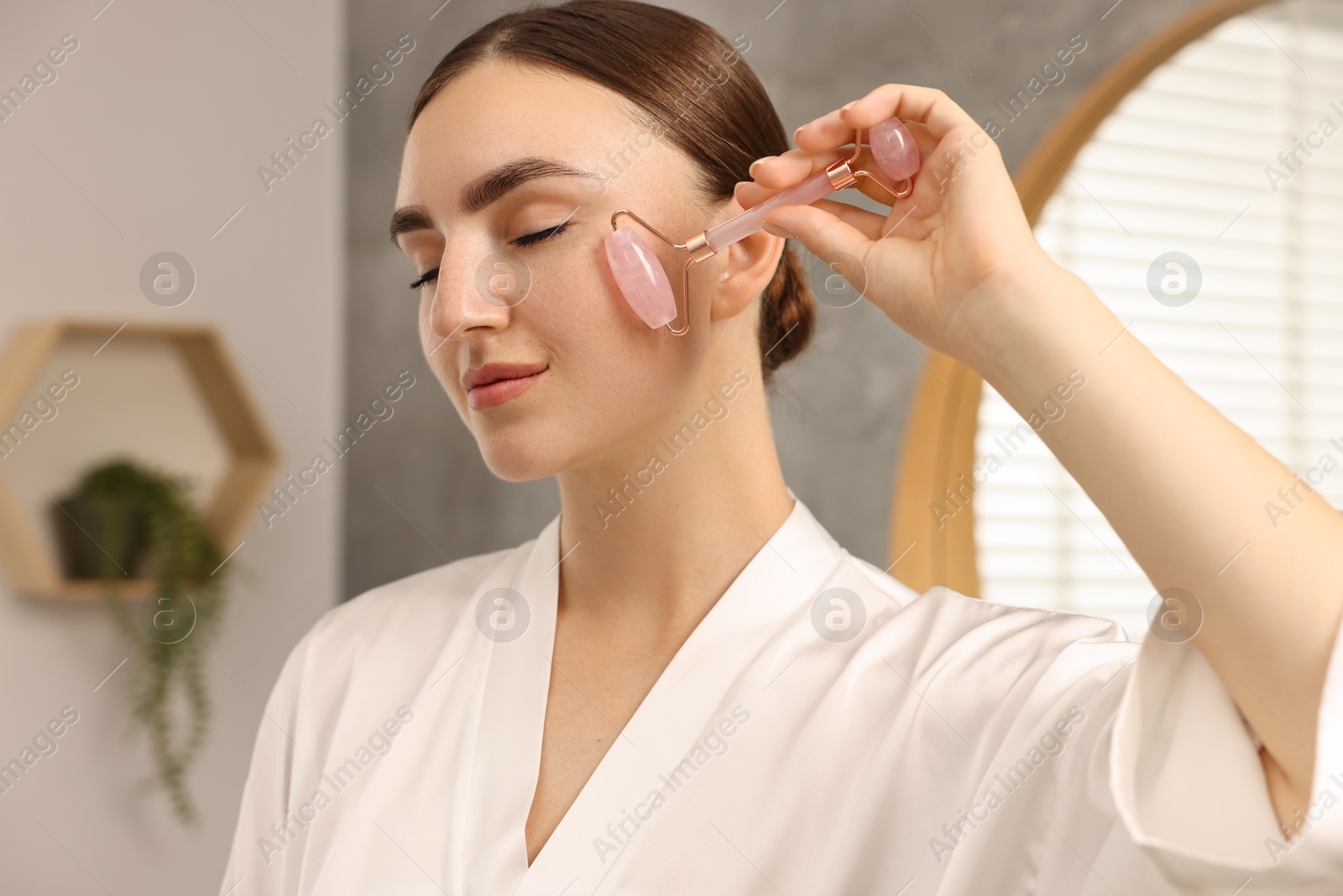 Photo of Beautiful young woman doing facial massage with roller at home