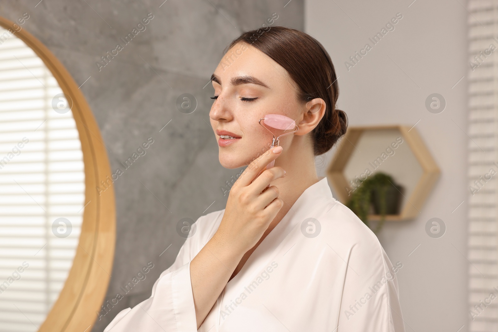 Photo of Beautiful young woman doing facial massage with roller at home