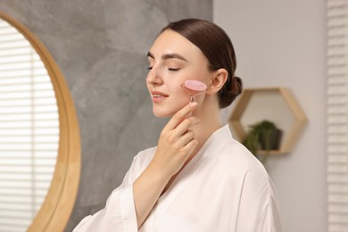 Photo of Beautiful young woman doing facial massage with roller at home