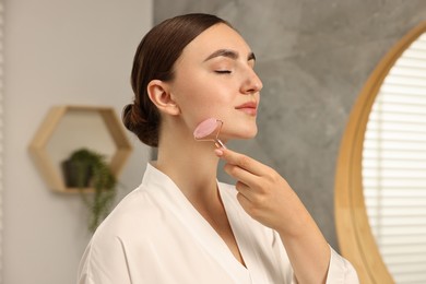 Photo of Beautiful young woman doing facial massage with roller at home