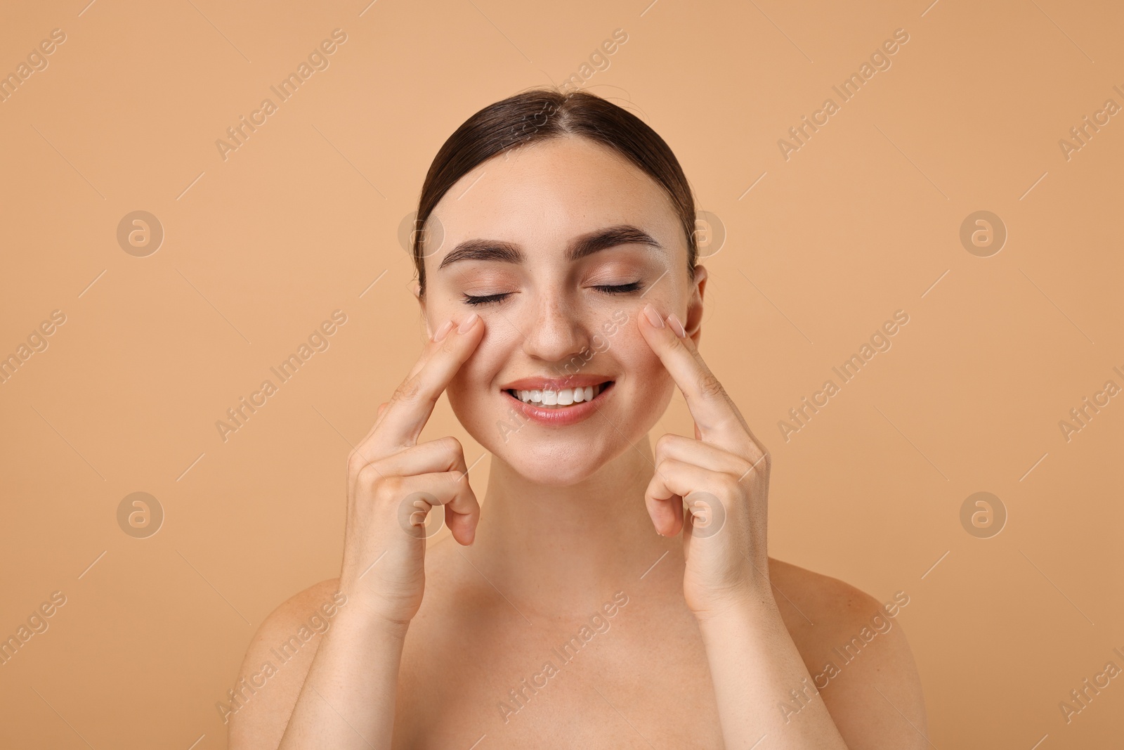 Photo of Beautiful young woman doing facial massage on beige background