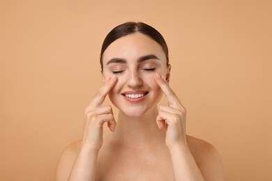 Beautiful young woman doing facial massage on beige background