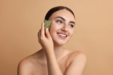 Beautiful young woman doing facial massage with gua sha tool on beige background