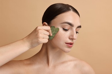 Beautiful young woman doing facial massage with gua sha tool on beige background