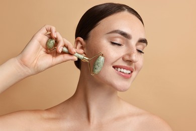 Beautiful young woman doing facial massage with roller on beige background