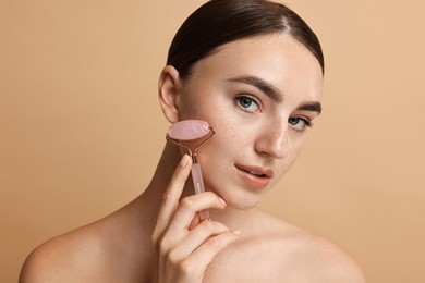 Photo of Beautiful young woman doing facial massage with roller on beige background