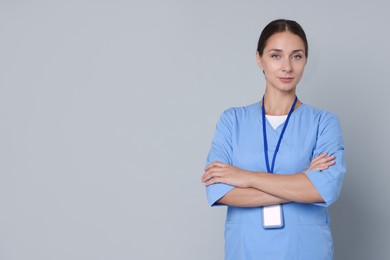 Nurse in medical uniform with badge on grey background, space for text