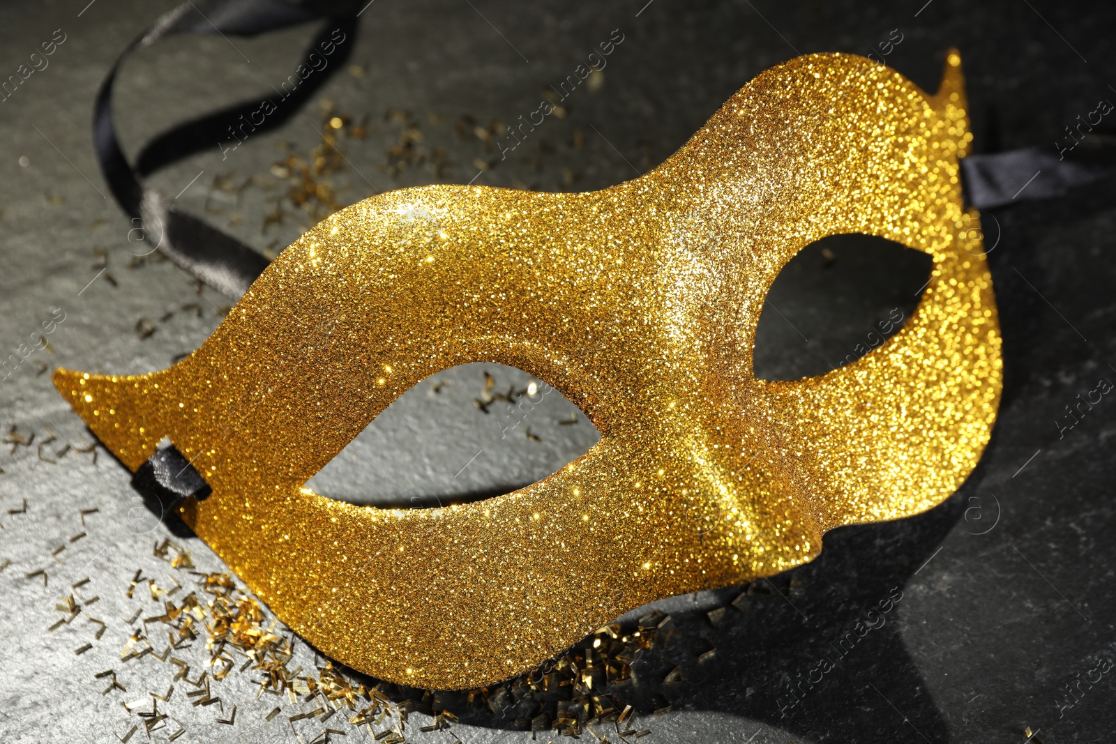 Photo of Beautiful golden carnival mask on grey textured table, closeup