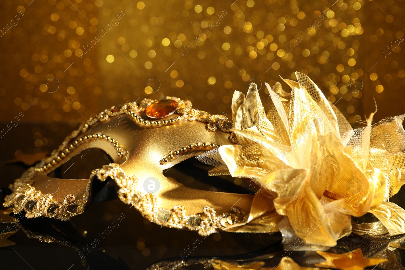 Photo of Beautiful golden carnival mask on mirror surface, closeup