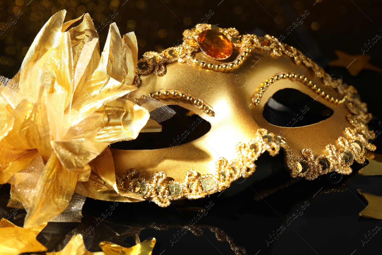 Photo of Beautiful golden carnival mask on mirror surface, closeup