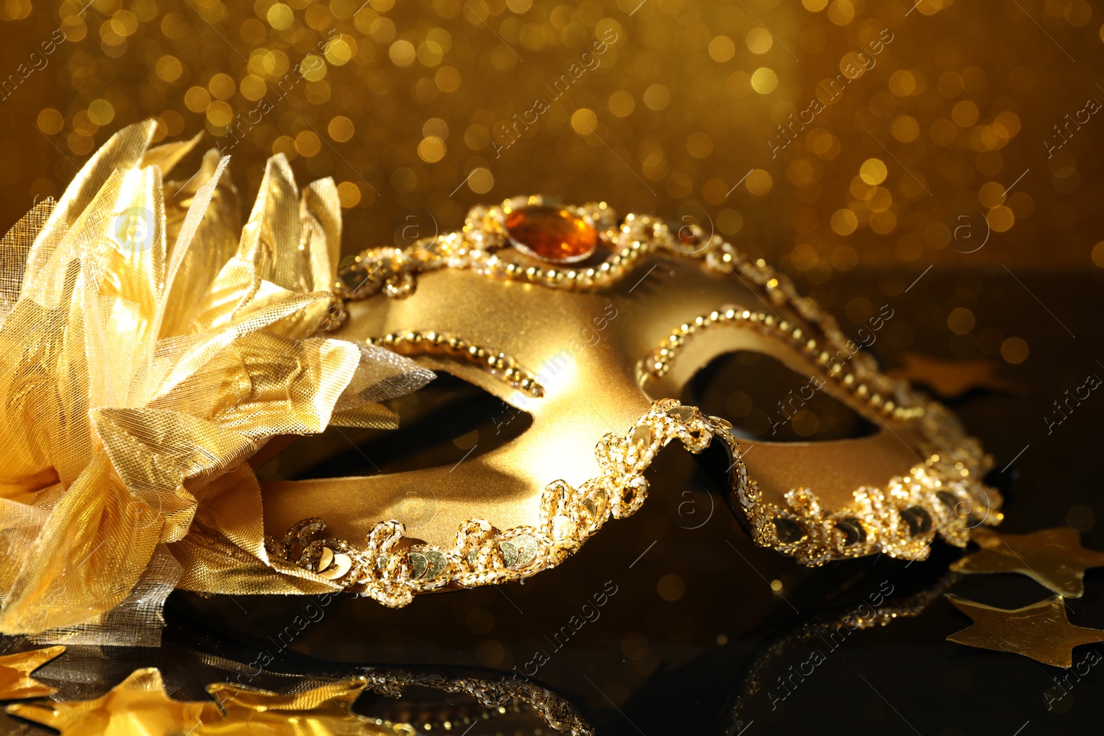 Photo of Beautiful golden carnival mask on mirror surface, closeup