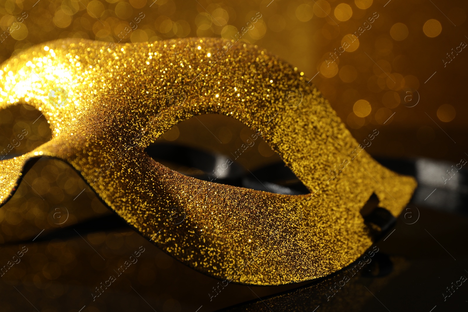 Photo of Beautiful golden carnival mask on mirror surface, closeup