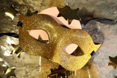 Beautiful golden carnival mask and decorative stars on table, top view