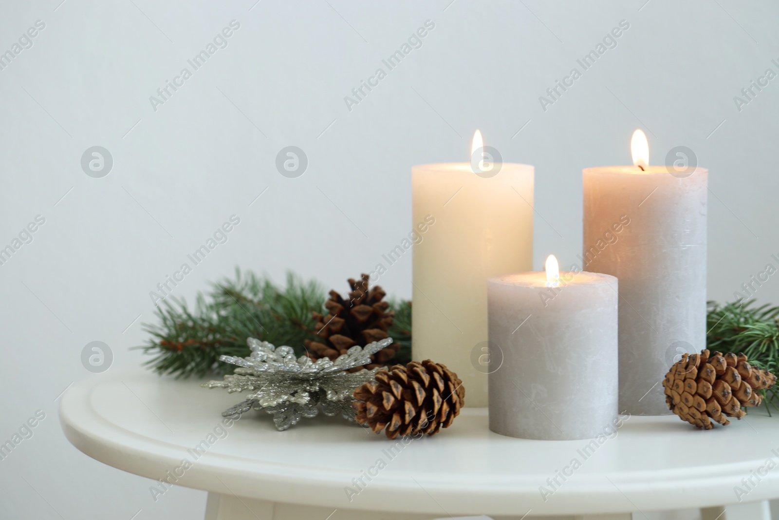 Photo of Burning candles and fir branches on coffee table near light wall, space for text