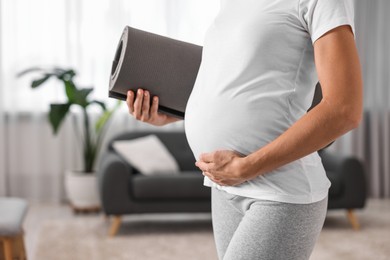 Pregnant woman with exercise mat at home, closeup