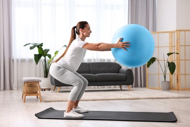 Beautiful pregnant woman doing exercises with fitball on mat at home