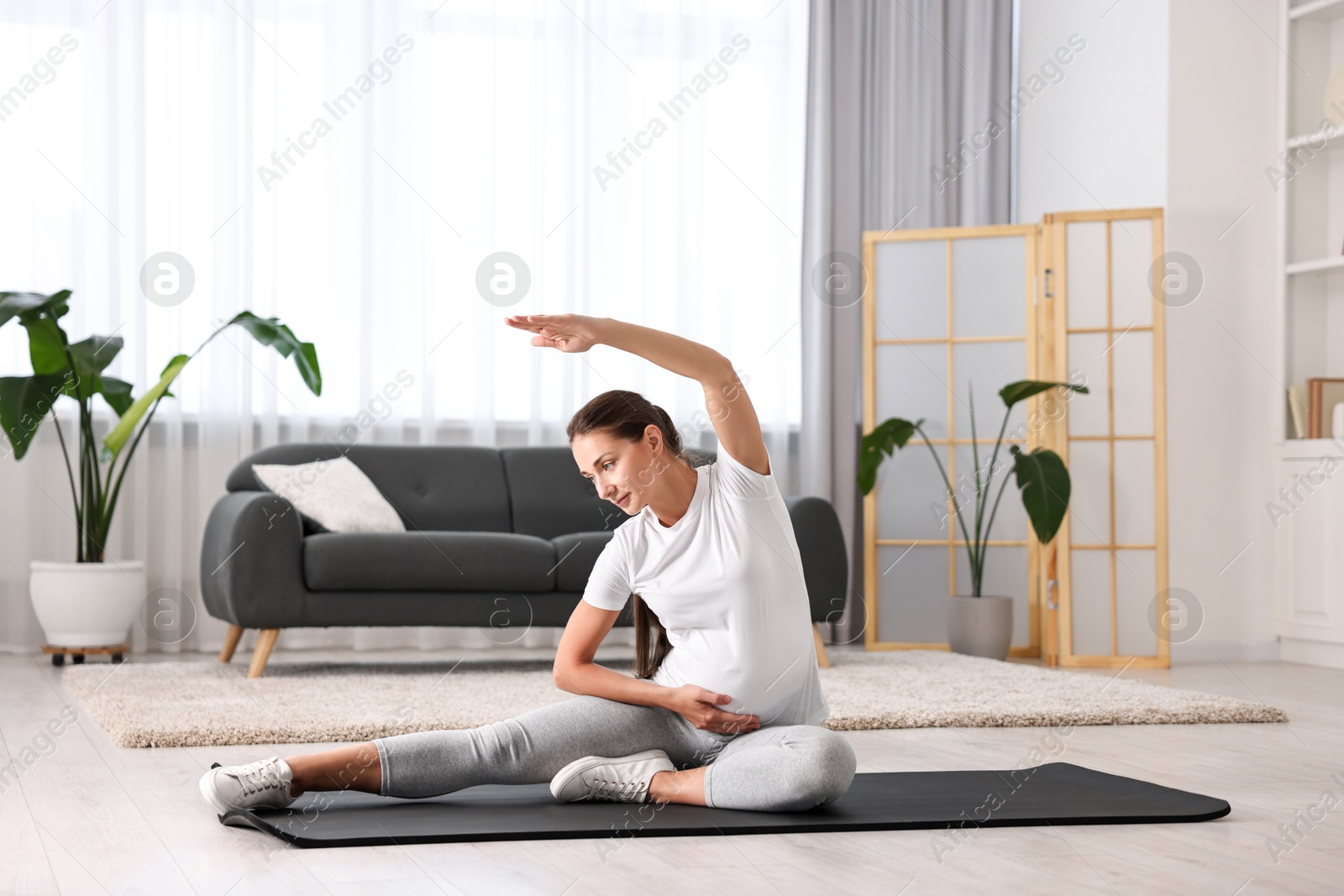 Photo of Beautiful pregnant woman doing stretching exercises on mat at home