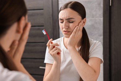 Photo of Young woman with toothbrush suffering from toothache in bathroom