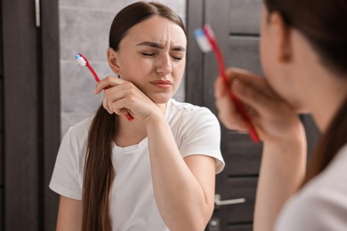 Photo of Young woman with toothbrush suffering from toothache in bathroom