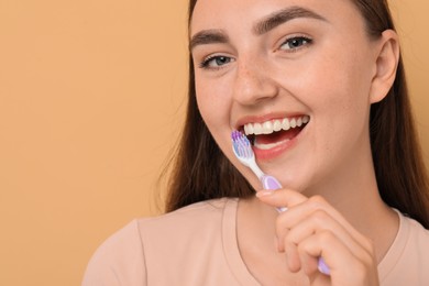 Photo of Beautiful woman brushing her teeth on beige background, space for text