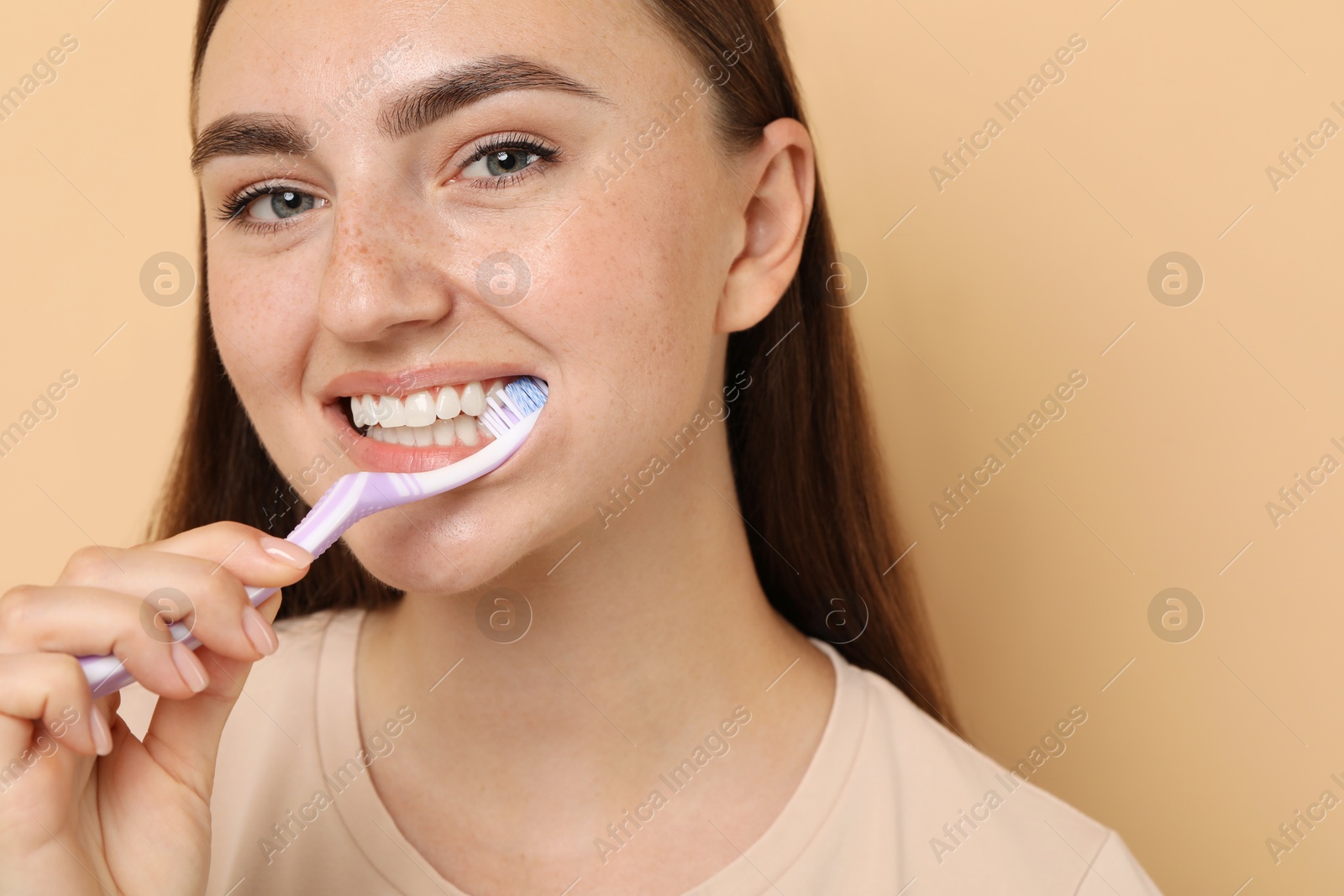 Photo of Beautiful woman brushing her teeth on beige background, space for text