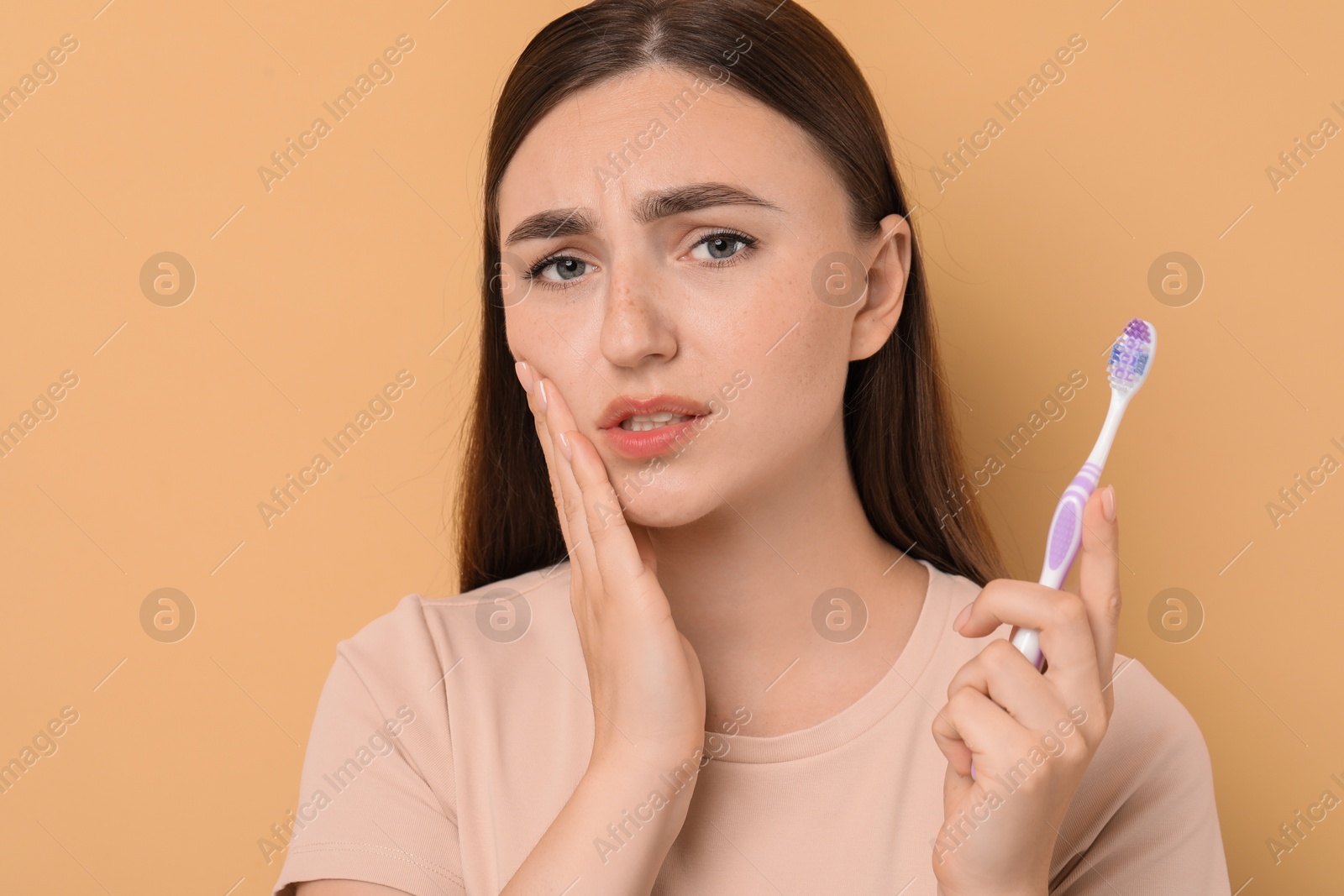 Photo of Young woman with toothbrush suffering from toothache on beige background