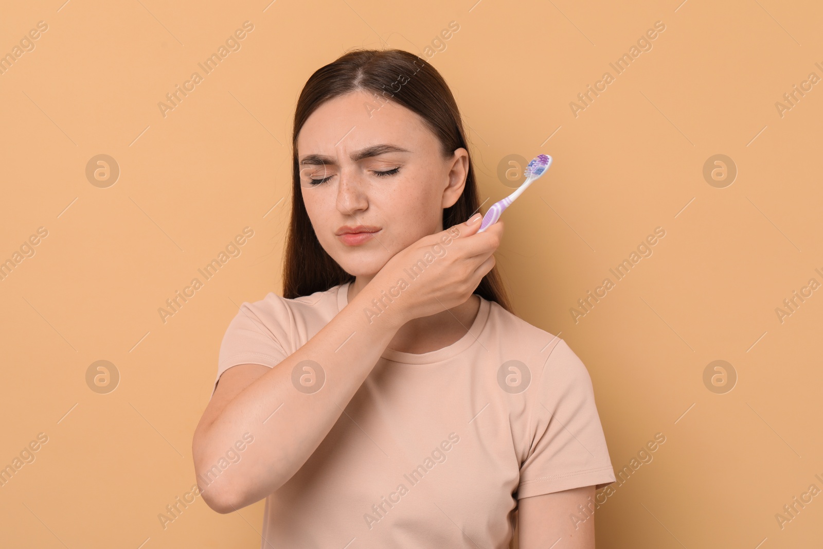 Photo of Young woman with toothbrush suffering from toothache on beige background