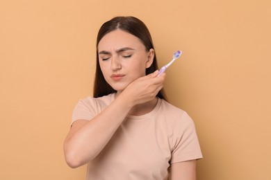 Young woman with toothbrush suffering from toothache on beige background