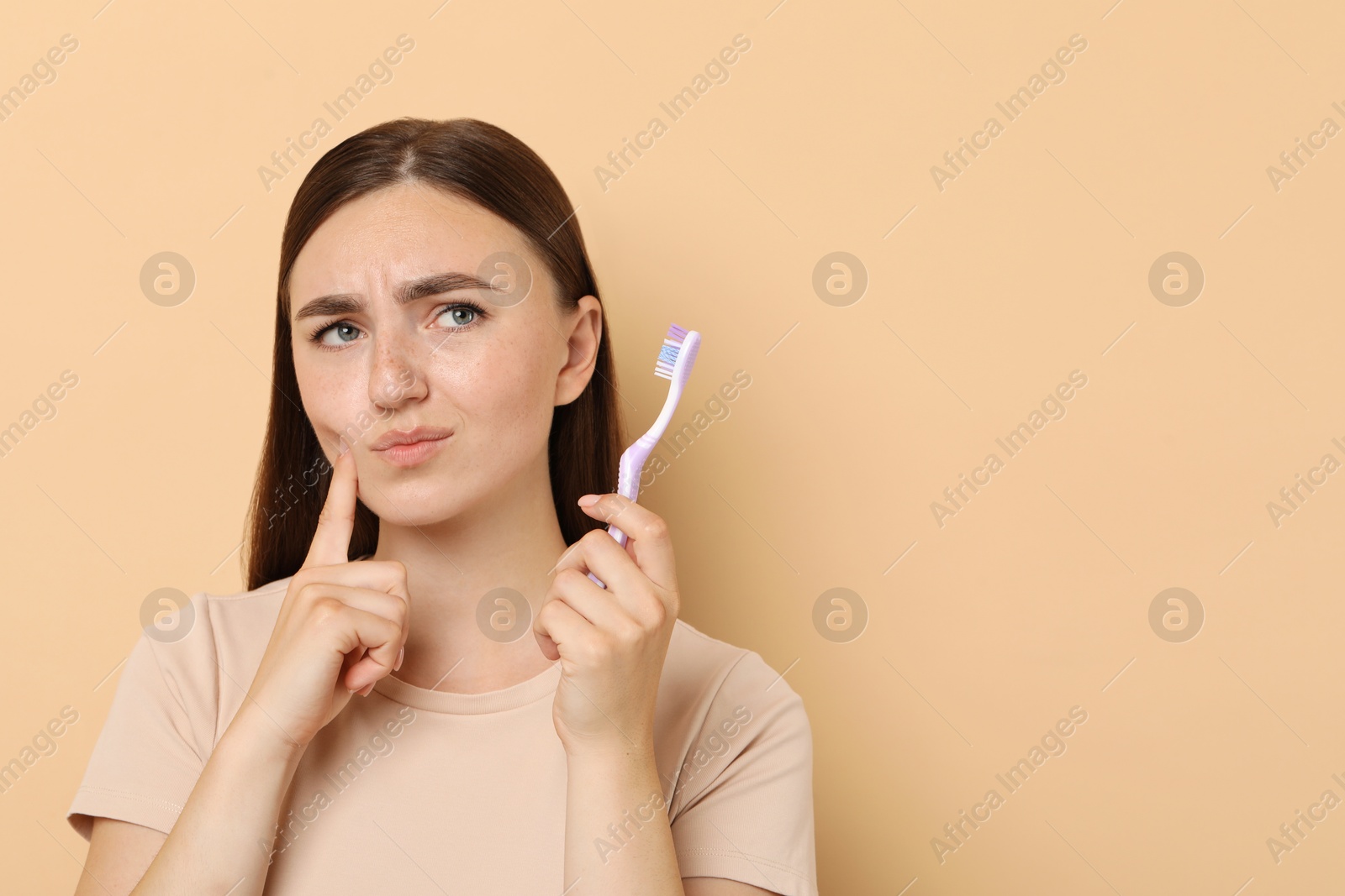 Photo of Young woman with toothbrush suffering from toothache on beige background, space for text