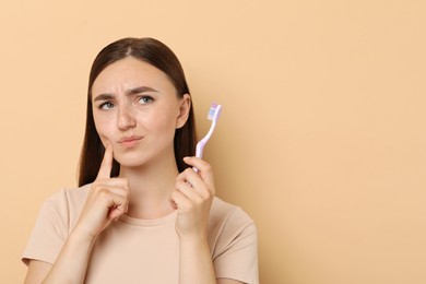 Photo of Young woman with toothbrush suffering from toothache on beige background, space for text