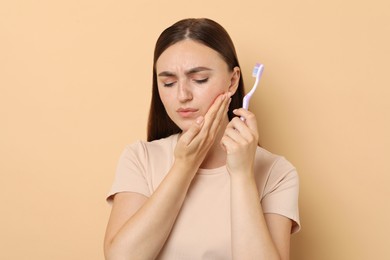 Photo of Young woman with toothbrush suffering from toothache on beige background