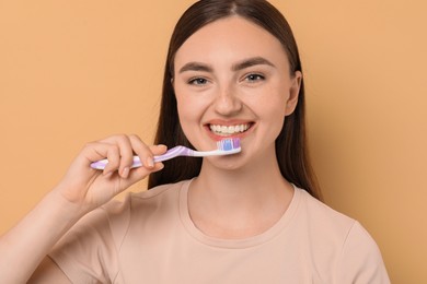 Beautiful woman brushing her teeth on beige background