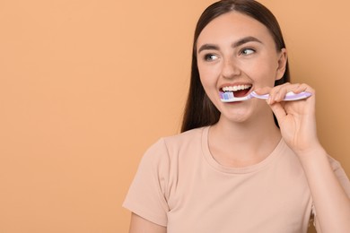 Beautiful woman brushing her teeth on beige background, space for text