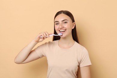 Beautiful woman brushing her teeth on beige background