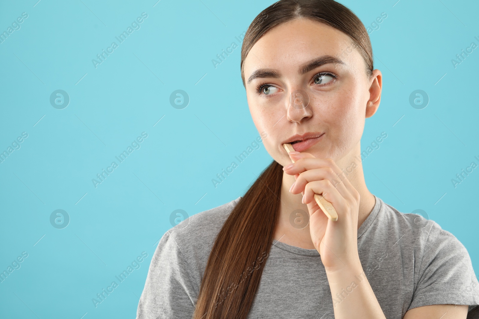 Photo of Beautiful woman brushing her teeth on light blue background, space for text