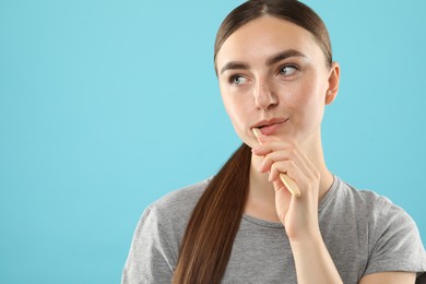 Beautiful woman brushing her teeth on light blue background, space for text