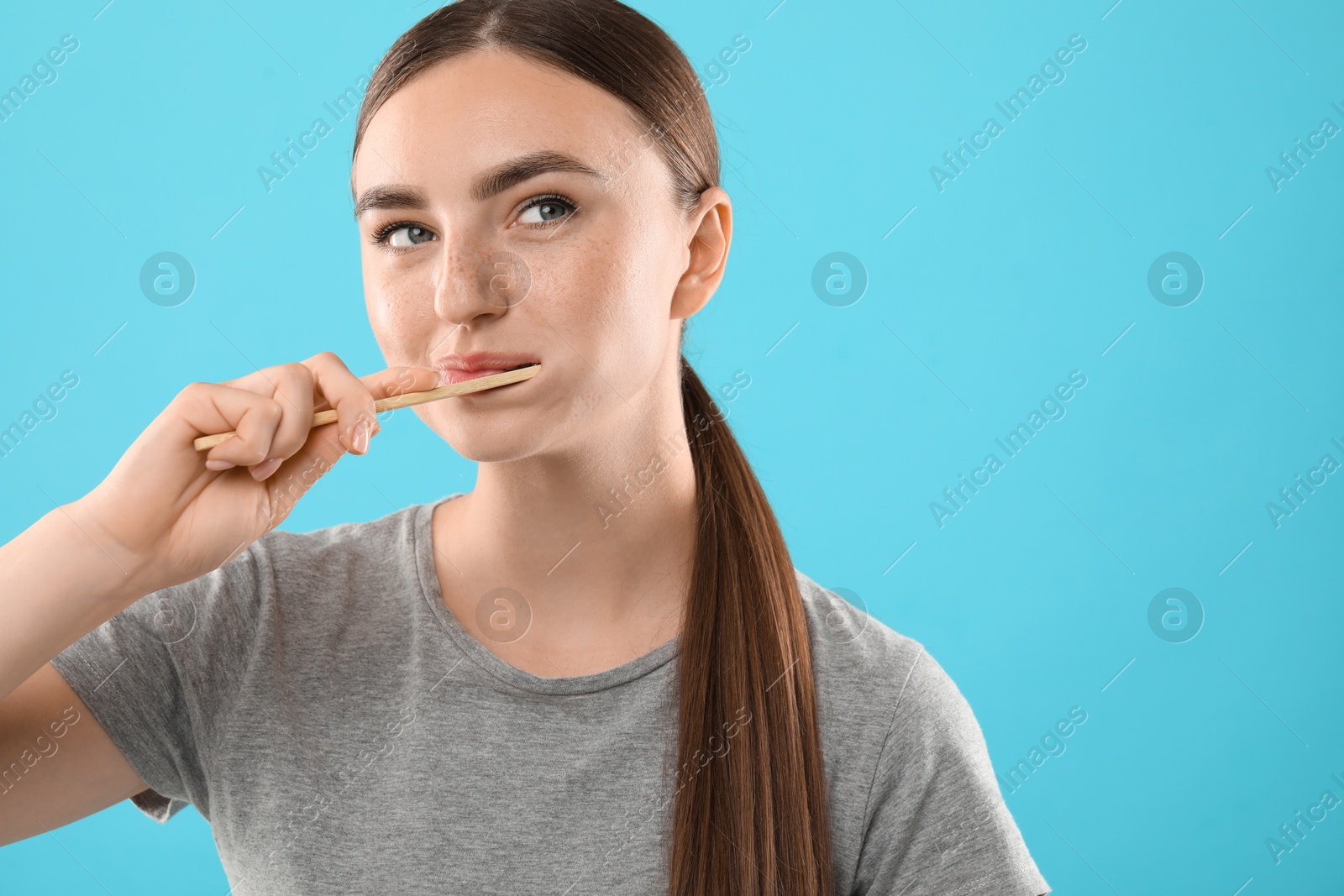 Photo of Beautiful woman brushing her teeth on light blue background, space for text