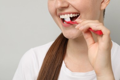 Woman brushing her teeth on gray background, closeup. Space for text