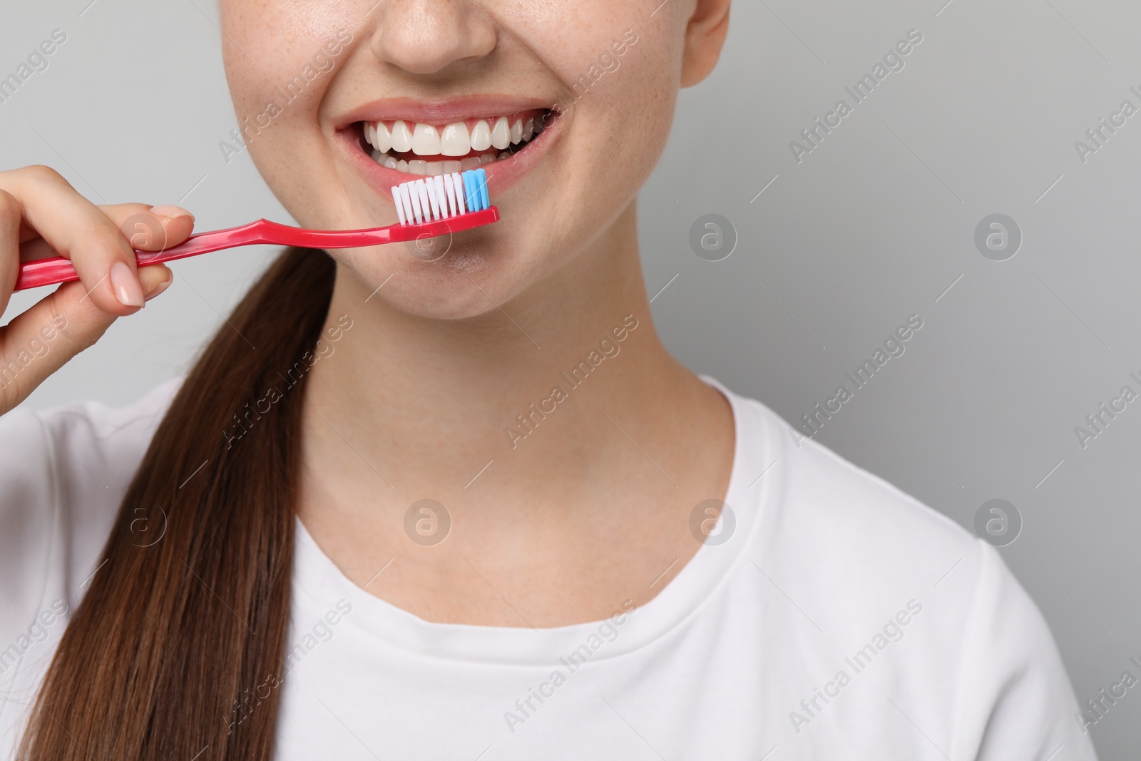 Photo of Woman brushing her teeth on gray background, closeup